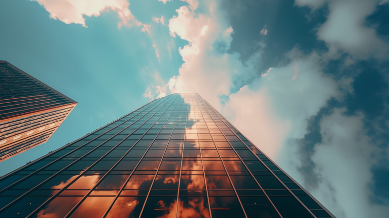 A towering skyscraper with a reflective glass facade, reaching into a sky filled with clouds illuminated by the warm glow of the sun.