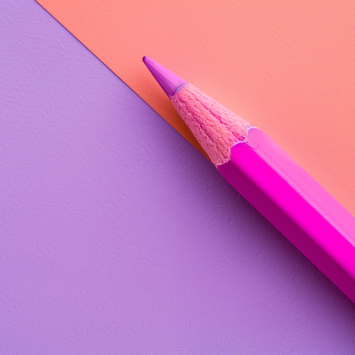 A purple colored pencil positioned diagonally along the boundary where a lavender surface meets an orange one, illustrating the concept of negative space.